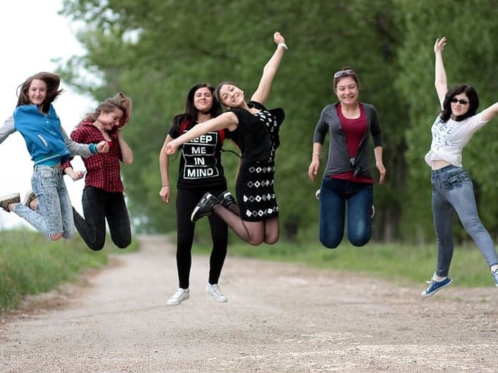 A group of girls jumping for a pose with forest in the background.